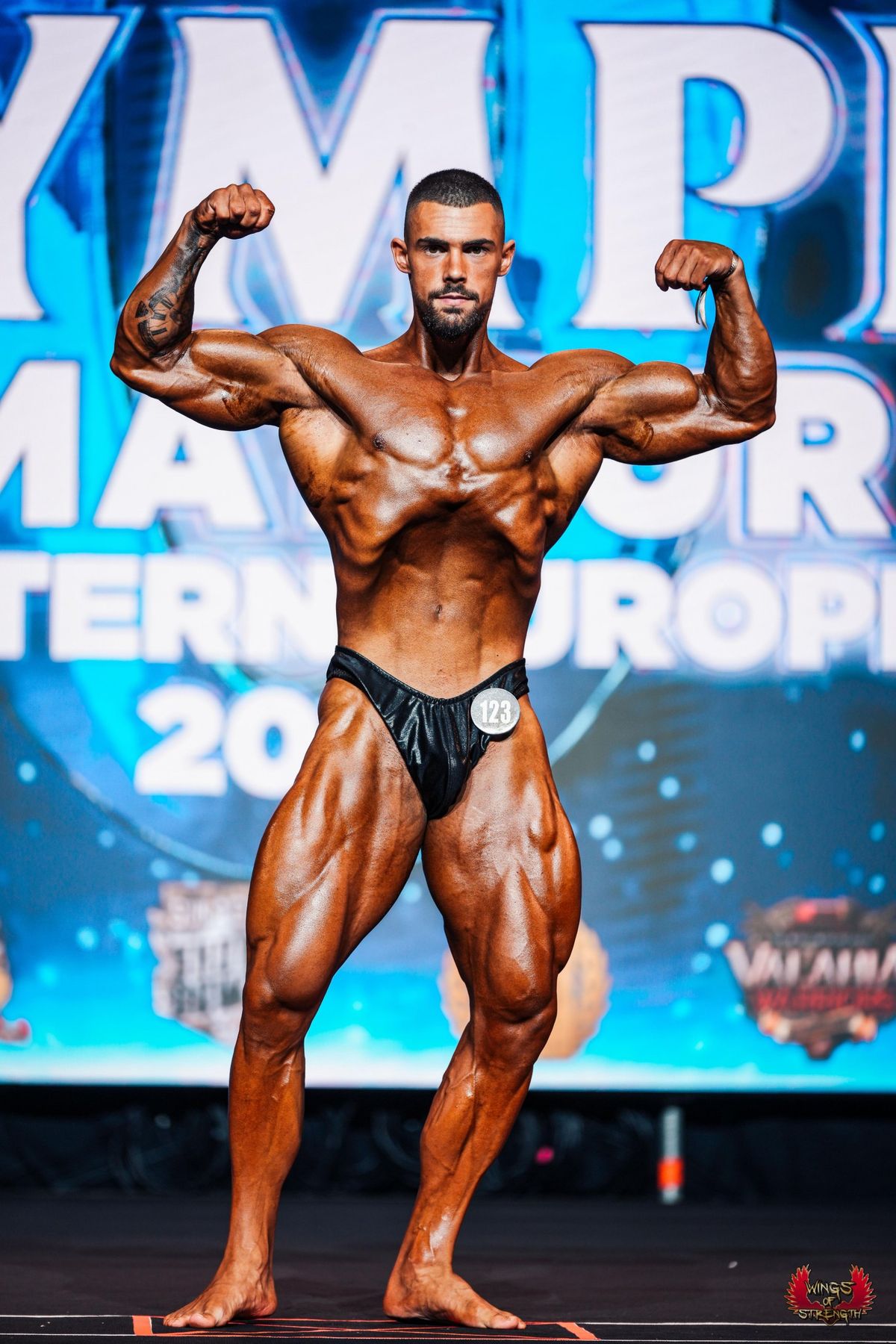 Alex Popa pe scenă, poză de concurs cu bicepșii încordați